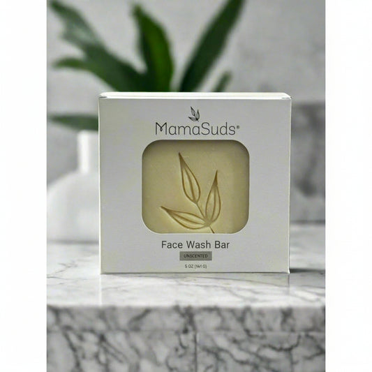 Mamasuds face wash bar packaging on a marble surface with a plant in the background